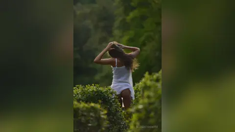 Dreamy portrait of a woman in a white summer dress standing in a lush green garden at sunset.