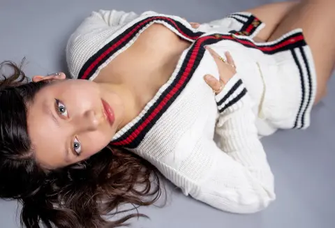 Young woman in a white knit cardigan with red and black stripes lying on a grey floor with a soft mood.