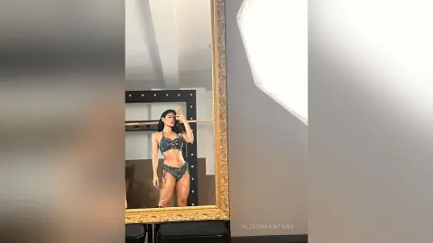 Confident woman in a grey bikini set posing for a mirror selfie in a bright, modern room.
