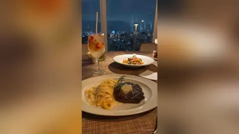 Gourmet steak and pasta dinner served on a table with a view of the city skyline at night.
