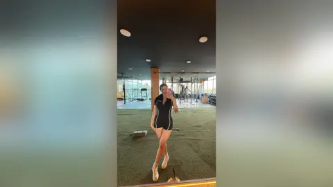 Athletic woman in black workout outfit taking a selfie in a modern bright gym setting.