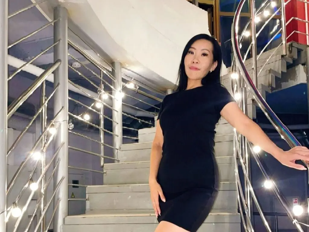 Elegant woman in a black dress standing on modern indoor stairs with bright decorative lights.