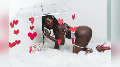 Sensual Black woman in white lace lingerie posing amidst white clouds and red heart decorations.