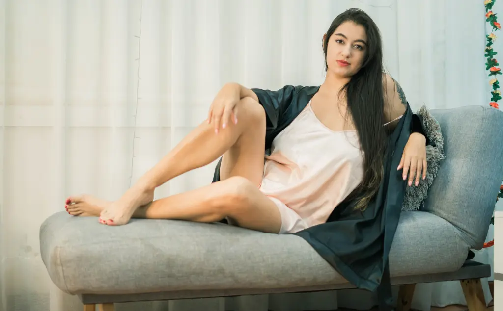 IvoneFisher poses in a black dress, running her hand through her long dark hair while sitting in a dim setting.