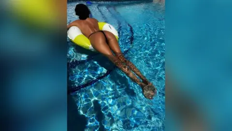 Relaxed woman in black bikini floating on a yellow pool float in a bright blue swimming pool.