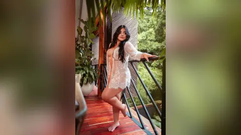 Elegant woman in a white lace robe relaxing on a tropical balcony overlooking lush green trees.