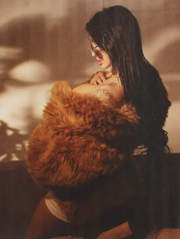 Stylish woman in a brown faux fur coat and sunglasses posing in warm, cinematic sunlight.