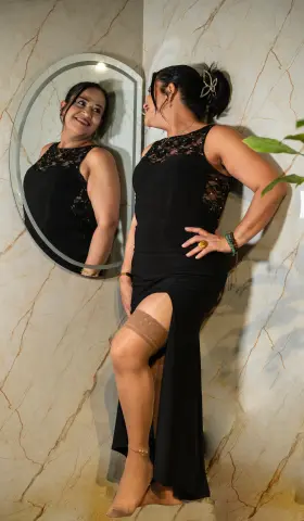 Smiling woman in a black sleeveless maxi dress with a side slit posing in a marble hallway.