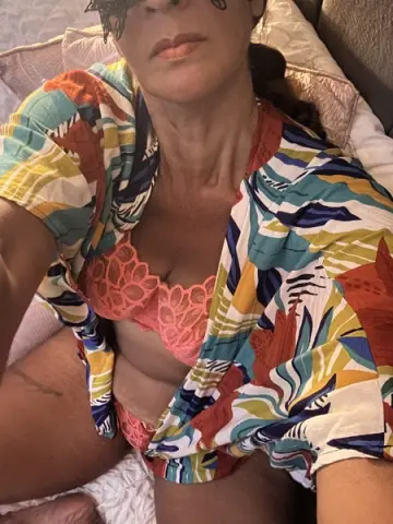 Woman in a colorful floral print shirt and pink lace lingerie relaxing on a bed.