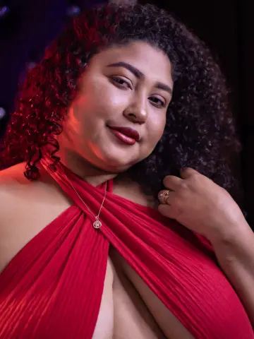 Smiling woman in a red halter dress wearing a silver necklace in a moody, dimly lit setting.