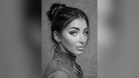 Portrait of a young woman with a messy bun wearing a denim jacket in a moody black and white studio setting.