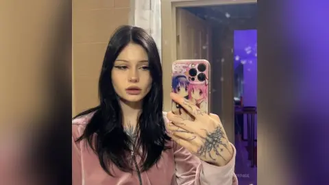 Young woman with long dark hair and lip piercing taking a moody selfie in a pink velvet top.