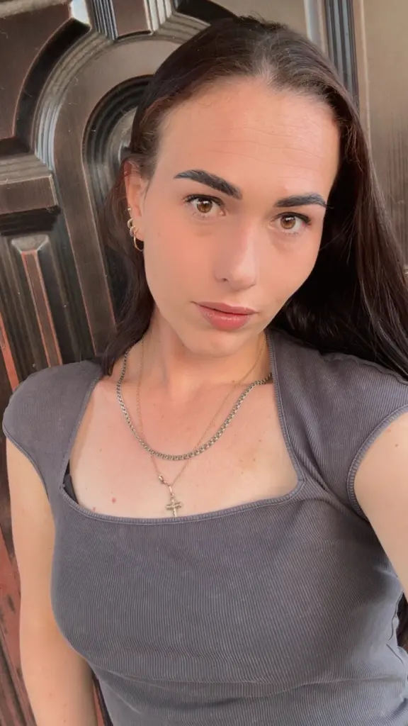 Close-up portrait of a woman with dark hair and gold hoop earrings posing against a vintage wooden door.