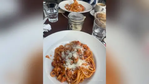 Delicious spaghetti bolognese topped with parmesan cheese served on a white plate in a cozy restaurant setting.