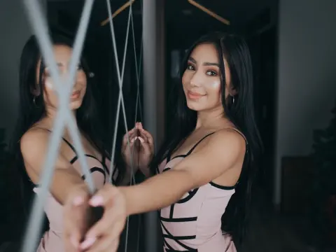 Smiling young woman in a pink spaghetti strap dress posing in front of a mirror in a dimly lit room.