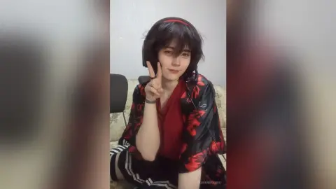 Young woman in a red and black floral kimono making a peace sign in a cozy indoor setting.
