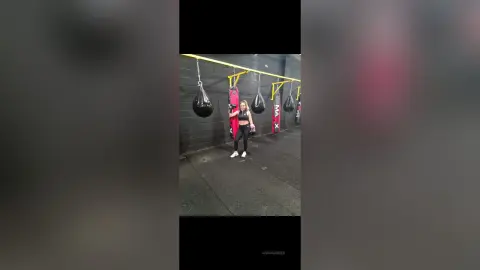 Fit woman in black gym wear training in a boxing gym with heavy punching bags hanging in the background.