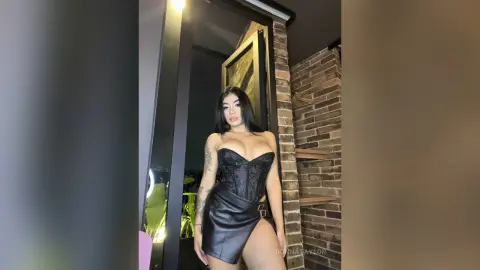 Glamorous woman in a black lace corset and leather mini skirt posing in a modern brick interior.