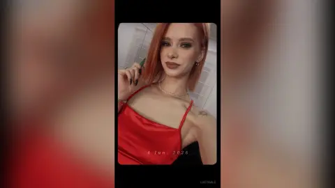 LucyGale poses in a red satin camisole, showing her shoulders and neck, with her red hair down and a pearl necklace.