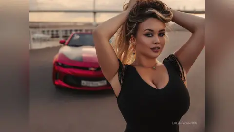 Beautiful woman in a black tank top posing confidently next to a red sports car at sunset.