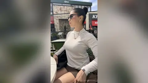 NashiroSakurai sits at an outdoor table wearing a white long-sleeve top and sunglasses with her hair in a bun.