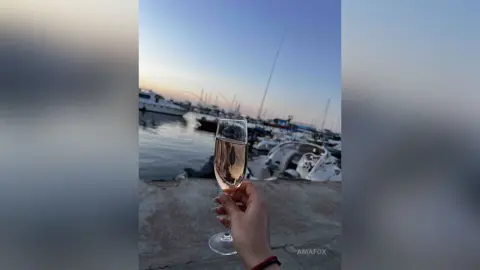 Hand holding a champagne flute at a luxury marina during a relaxing sunset by the yachts.
