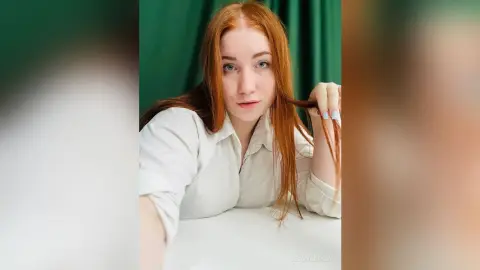 Redheaded woman in a white button-down shirt posing against a green curtain background with a soft mood.