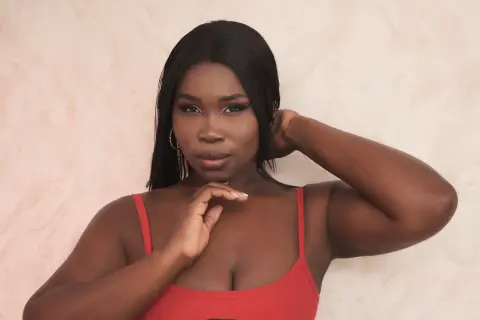 Beautiful Black woman in a red tank top posing against a neutral textured background with a confident mood.