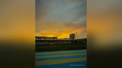 Golden sunset sky over a modern stadium building and athletic running track at dusk.