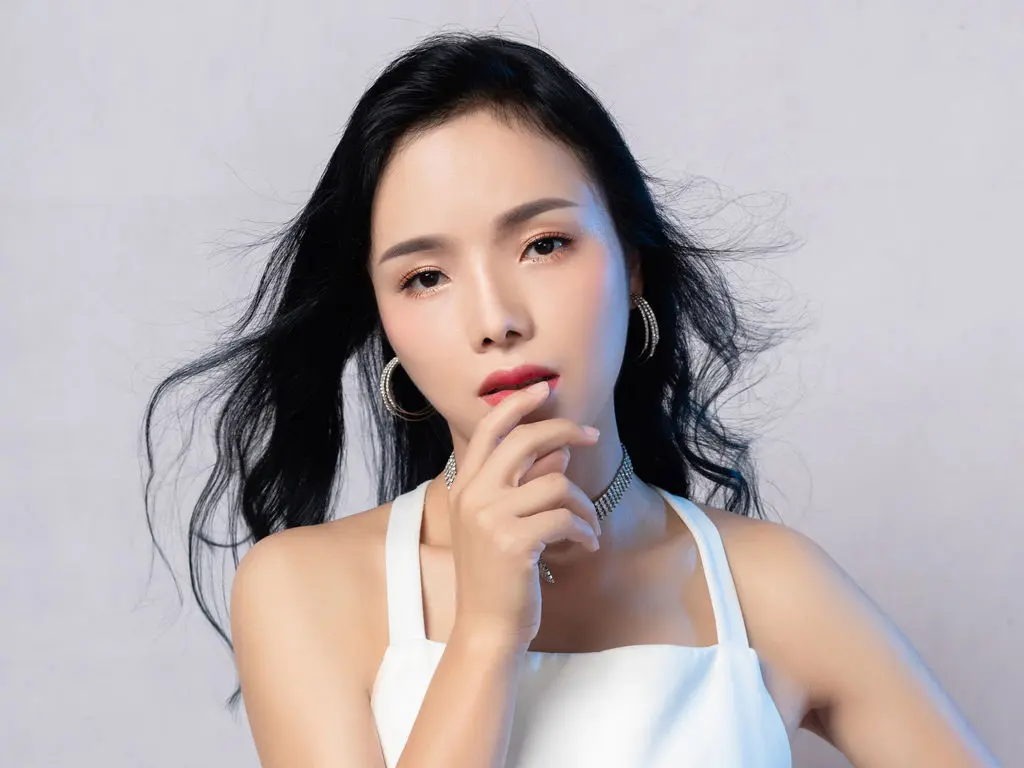 Elegant woman with long black hair in a white tank top posing against a light studio background.