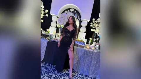 Elegant woman in a black evening gown posing at a glamorous floral event with sparkling decor.