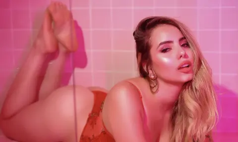 Glamorous blonde woman in orange lace lingerie relaxing in a pink tiled bathroom with a dreamy mood.