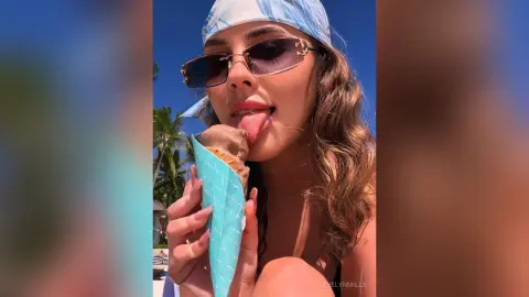 Smiling woman in sunglasses and blue bandana enjoying a melting ice cream cone on a sunny summer day.