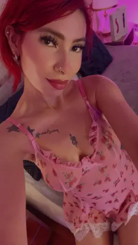 Woman with red hair in pink floral lace camisole relaxing in a bedroom with warm lighting.