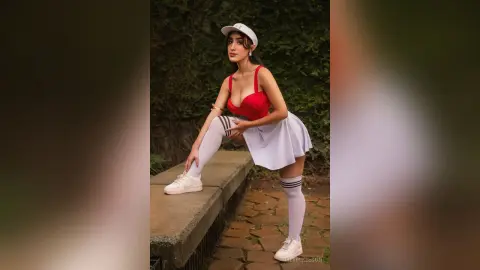 Young woman in a red crop top and white tennis skirt posing outdoors in a stylish sporty outfit.