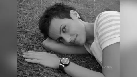 Smiling woman in a striped t-shirt relaxing on the grass in a peaceful black and white outdoor portrait.