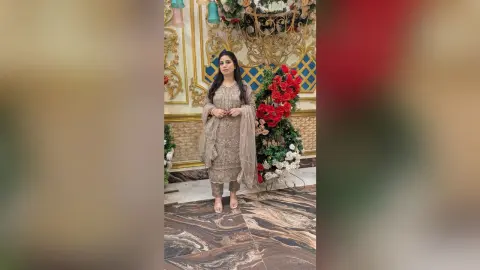 Elegant woman in a shimmering grey ethnic salwar kameez standing in a luxurious floral decorated room.