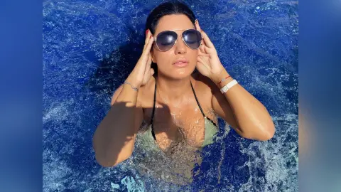 MissyJolie wears dark sunglasses and a light green bikini while relaxing in bright blue swimming pool water.