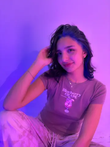 Young woman in a blueberry graphic t-shirt posing under dreamy purple neon lighting.