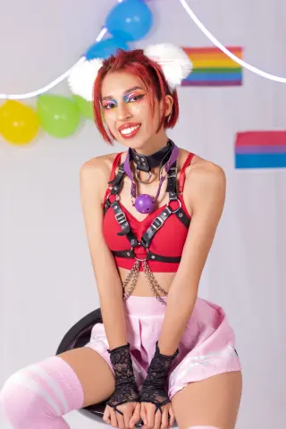 Smiling woman in red cosplay outfit and pink skirt posing against colorful balloons in a bright studio.