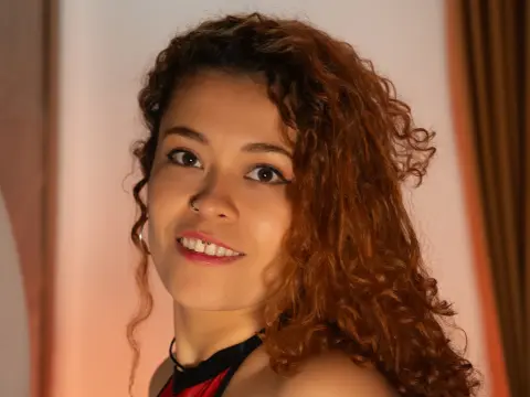 Smiling young woman with curly brown hair wearing a black halter top in a warm indoor setting.