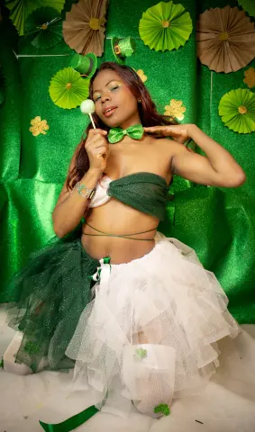 Glamorous woman in a green and white sparkly tutu outfit posing against a festive green glitter background.