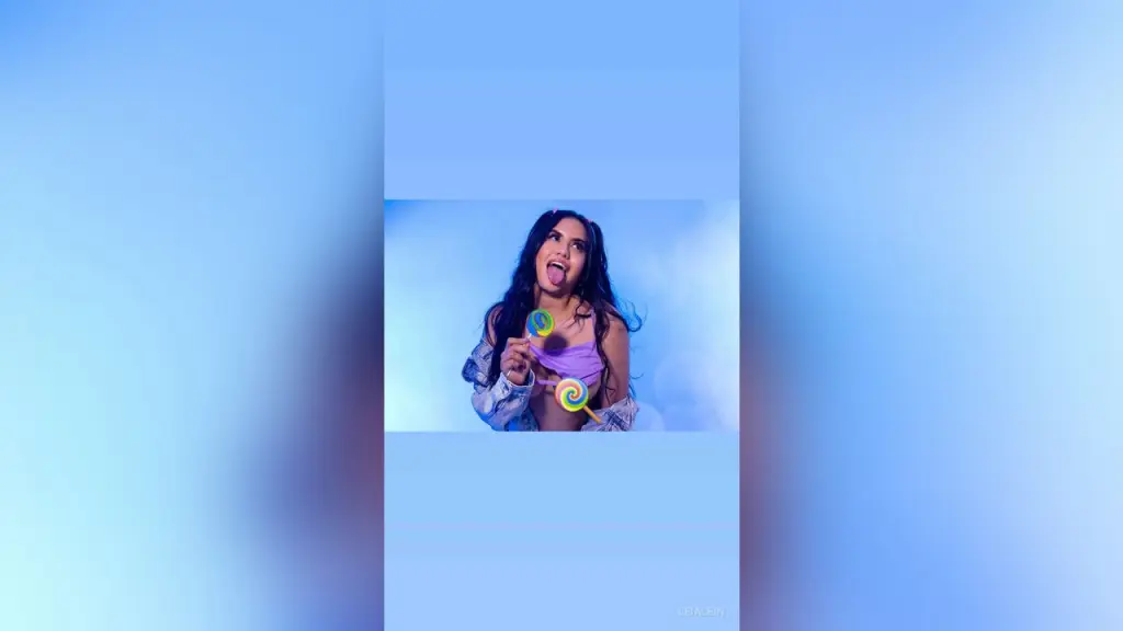 LeiaLein — Cheerful young woman in a purple top holding lollipops against a dreamy blue misty background.