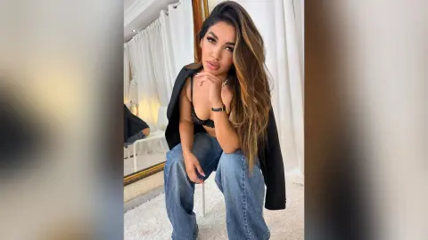 Stylish woman in a black blazer and jeans posing confidently in a bright, modern room.
