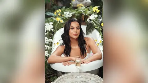 Elegant woman in a white dress relaxing in a garden bathtub surrounded by white and yellow flowers.