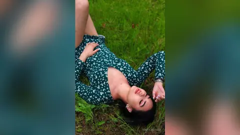 Young woman in a floral green long-sleeve dress relaxing on lush green grass in a peaceful outdoor setting.