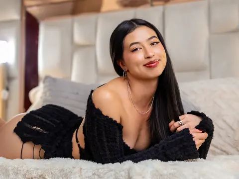 Smiling woman in a black fuzzy lounge outfit relaxing on a cozy white bed in a bright bedroom.