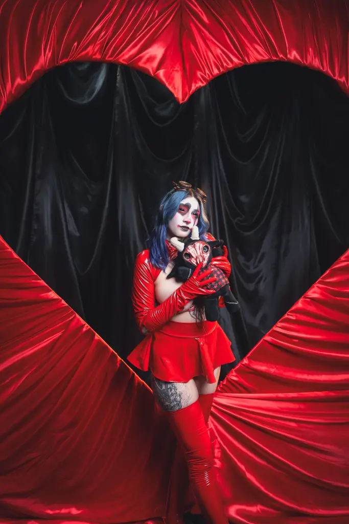 KimLennoxc with blue hair and glasses wears a black top while posing in front of a spooky spiderweb backdrop.