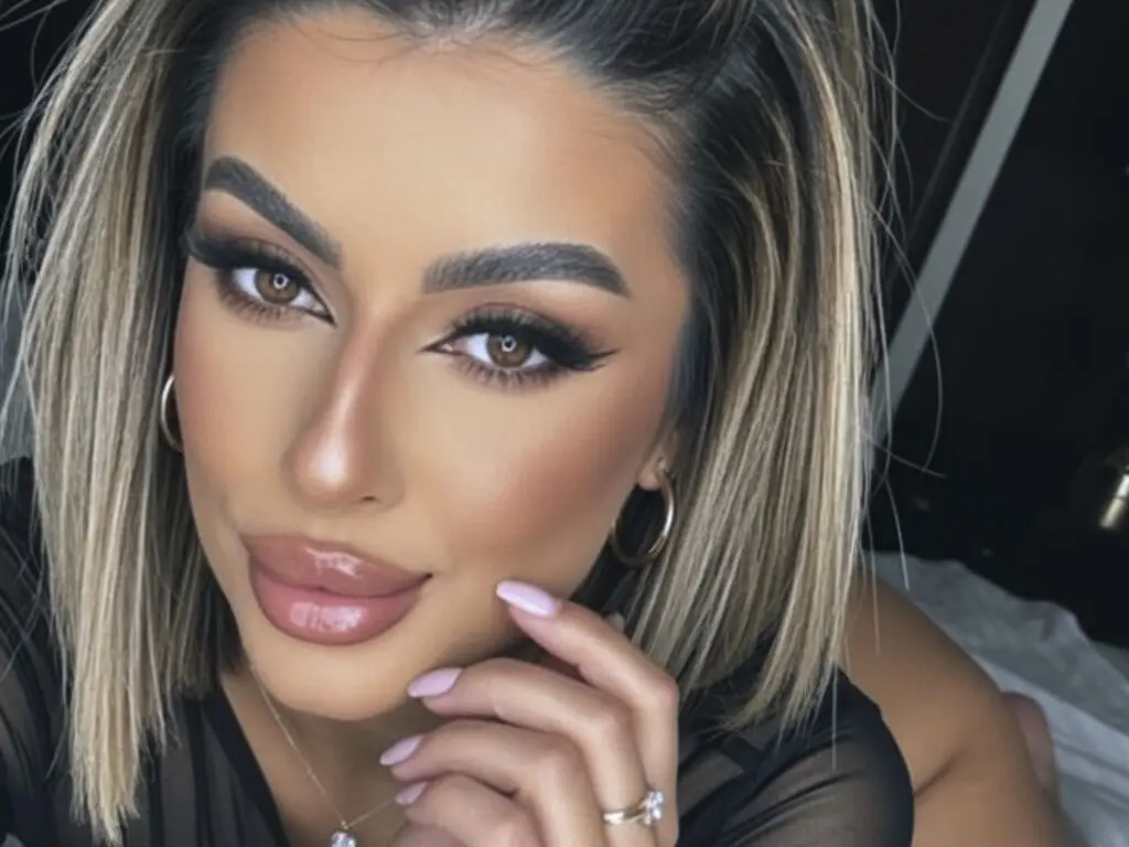 SinnaRay poses for a close-up selfie, looking into the camera with her blonde-streaked hair and heavy makeup.