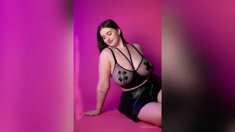 Curvy woman in black mesh lingerie and leather skirt posing against a vibrant pink studio background.